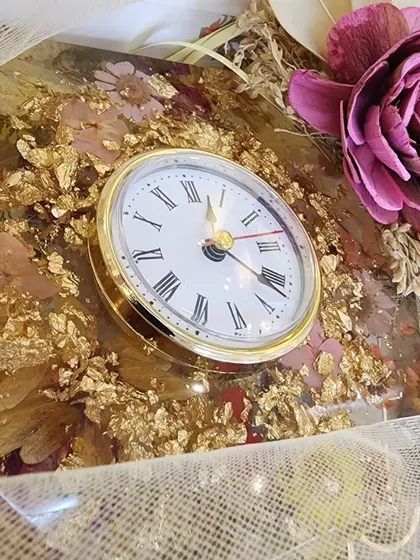 This handmade resin desk clock was created with dried flowers and gold flakes for a client's office. The 8-inch hexagonal clock has a silent mechanism, making it a stylish and peaceful addition to any workspace.