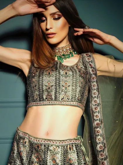 A mid-shot capturing a dynamic pose that highlights the model's toned midriff and the detailed embroidery on the lehenga. It's a modern and confident take on ethnic fashion photography.