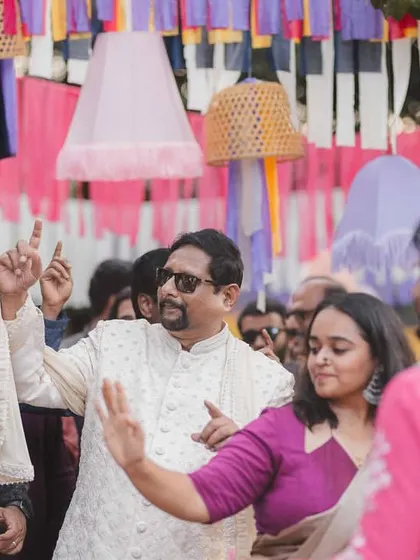 Guests dancing with abandon during the Baraat at a vibrant destination wedding. The colorful overhead decor with ribbons and cane baskets added to the festive atmosphere.