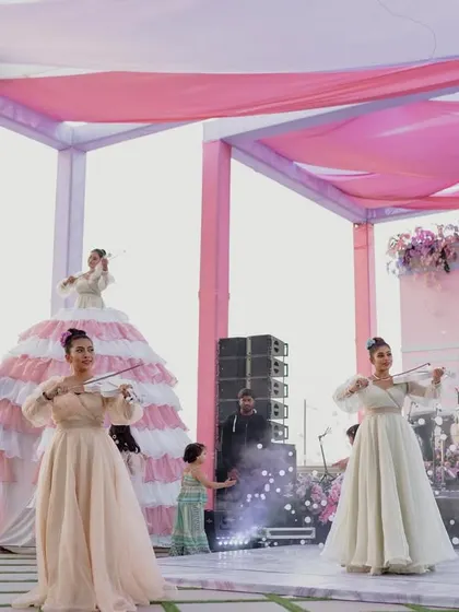 Performers playing the violin, including one on a whimsical tiered dress, serenade guests, perfectly capturing the romantic and theatrical spirit of Bridgerton.