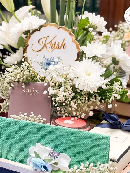 A personalized hamper for "Krish," filled with curated gifts from Jo Malone and Entisi, surrounded by a lush bed of fresh white flowers. It shows how we tailor each gift to the individual.