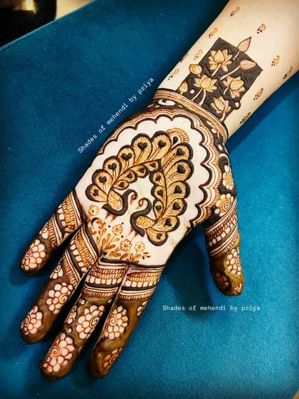 An intricate design featuring a heart shape made of two peacocks. The wrist has a modern 'negative space' or cutwork design with lotus flowers.