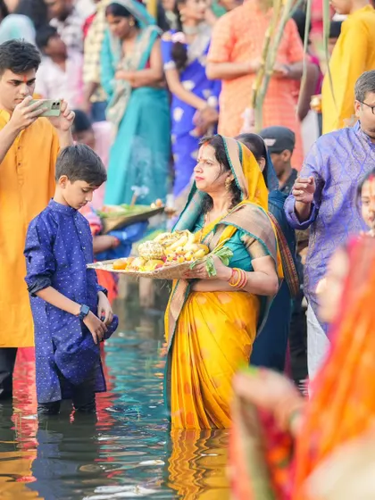 A family participates in Chhath Puja, with a woman holding a tray of offerings. It is a beautiful tradition that is passed down through generations.