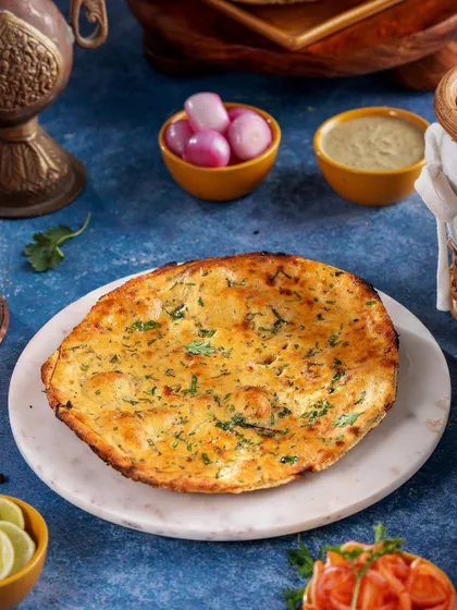 A perfectly cooked, golden-brown garlic naan served on a marble platter. The image is styled simply to let the texture and aroma of the tandoori bread speak for itself, complemented by traditional Indian pickles.