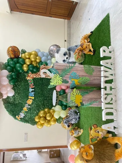 A top-down view of a jungle-themed setup with a faux grass backdrop. The decor is rich with stuffed animals like a lion, panda, and zebra.