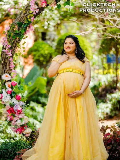 A radiant mother-to-be in a beautiful yellow gown, framed by a rustic floral arch in our garden.