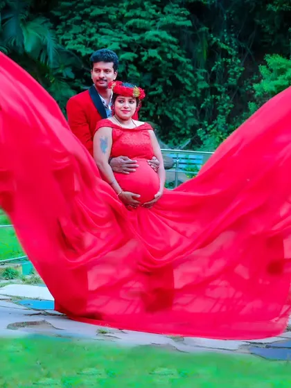 A dramatic maternity photo where the flowing red fabric of the gown creates a wing-like effect around the couple.