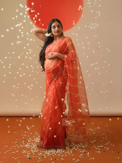 A full length portrait showcasing the sheer elegance of the orange saree. Her pose is confident and serene, a beautiful tribute to her pregnancy journey.