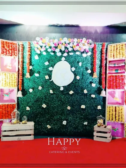 A creative backdrop for a baby shower, combining a central green wall with a Ganesha silhouette and side panels made of colorful fabric and marigold flowers.