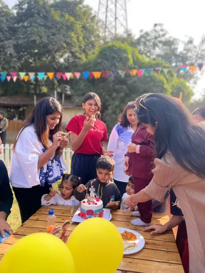 A candid shot of a birthday celebration, with children gathered around the table to help the birthday boy cut his cake.