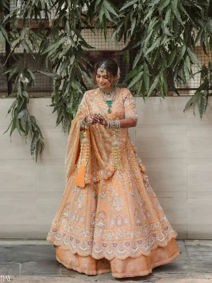 A full-length portrait of the bride in her peach lehenga, showcasing her traditional kaleeras.