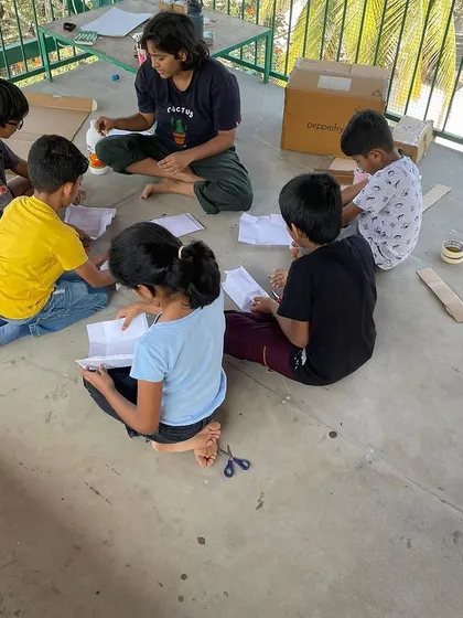 Children working together, cutting and gluing materials to build their models. This month-long project involved research, interviews, and hands-on artistic creation.