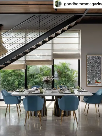 The dining area in the Dua Residence, set against a backdrop of lush greenery visible through floor-to-ceiling windows. The vibrant blue chairs add a beautiful pop of color to the otherwise neutral and serene space.