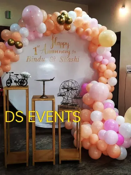 A lovely pastel-themed backdrop for a first anniversary celebration. The asymmetrical balloon arch in shades of peach, pink, and white adds a soft and romantic touch to the couple's special day.