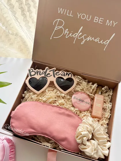 Propose to your bridesmaids with this curated gift box. It includes fun 'Bride Team' sunglasses, a silk eye mask for relaxation, a scrunchie, and a personalized badge, all ready to surprise your girl gang.
