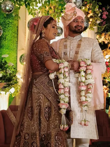 A beautiful moment from a couple's Varmala ceremony, set against a lush green backdrop with sparkling disco balls.
