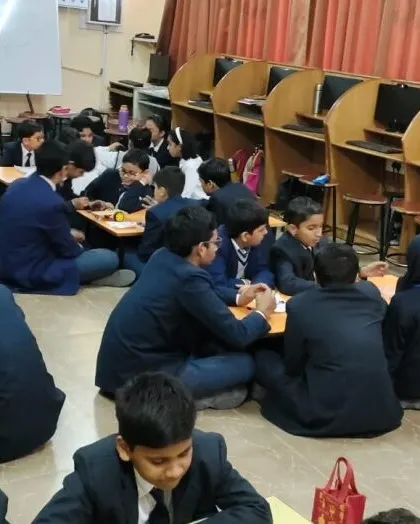 A wide view of a robotics workshop in session, with students sitting in groups and actively working on their projects.