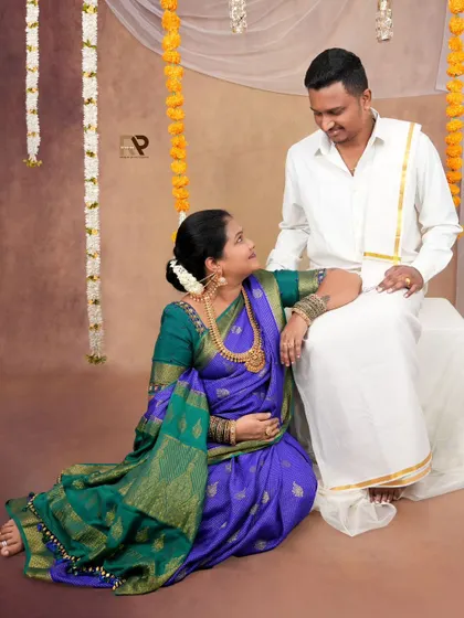 An intimate moment between the couple, dressed in traditional South Indian attire. The floral garlands and simple backdrop create a festive and authentic atmosphere.