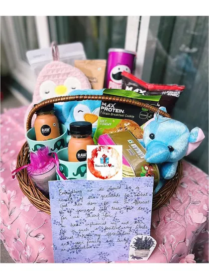 An open view of a family gift basket, showcasing the contents. This hamper is filled with snacks like Pringles, healthy cookies, drinks, plush toys, and a handwritten personal note for that extra special touch.