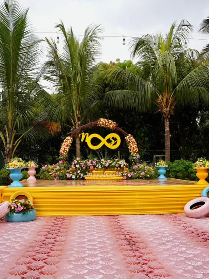 A modern and playful Mehendi stage. The infinity symbol with the couple's initials, set against a bright yellow stage, symbolizes their forever love story in a fun and contemporary way.