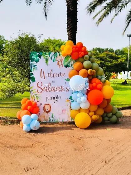 An outdoor welcome sign for a jungle-themed party, framed by a balloon garland in bright, sunny colors.