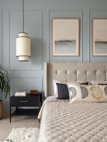 In the Neutral Chic home, the master bedroom features a serene dusty blue paneled wall. The tufted wingback headboard and layered textiles add a touch of classic elegance and comfort.