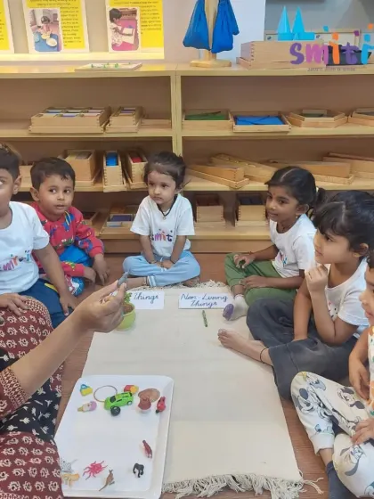 A group of children listens intently as their teacher explains the difference between a toy car and a real insect. This activity encourages critical thinking and observation skills.