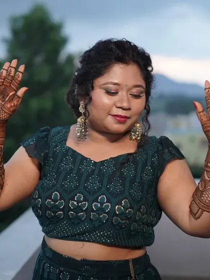 A happy bride showing off her intricate mehendi. The design covers her hands and forearms with traditional patterns that look stunning with her festive attire.
