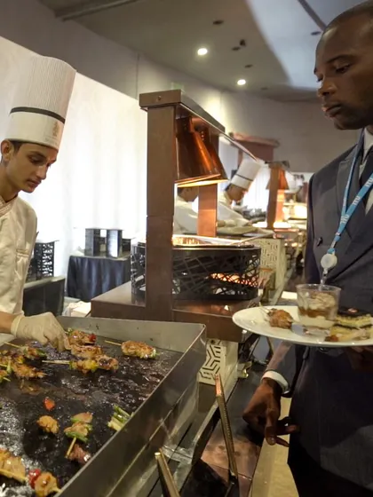 A guest selects freshly grilled skewers from a live station. The direct interaction and the sight of food being cooked to order adds an element of excitement and freshness.