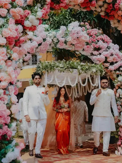 A breathtaking entrance through a tunnel of flowers. The bride looks like a vision in her traditional saree, creating a truly magical wedding moment.