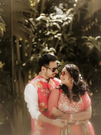 A cozy and intimate embrace. The couple holds each other close, sharing a quiet moment away from the crowd, framed by the lush greenery of the venue.