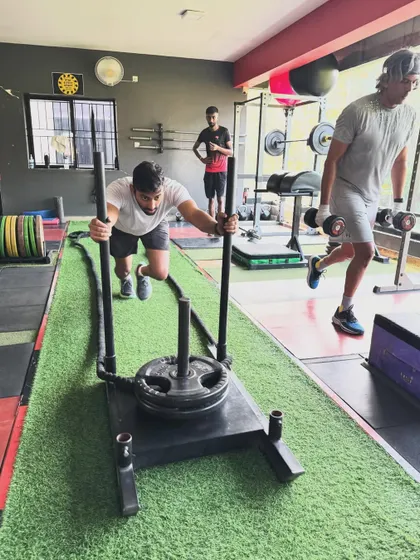 A client pushes a sled while another performs walking lunges, a perfect example of a challenging workout combination.