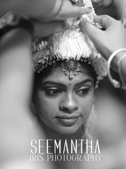 A powerful black and white close-up of a woman during her Seemantha ceremony. The focus is on her expressive face as hands perform a traditional ritual, capturing the solemnity of the moment.
