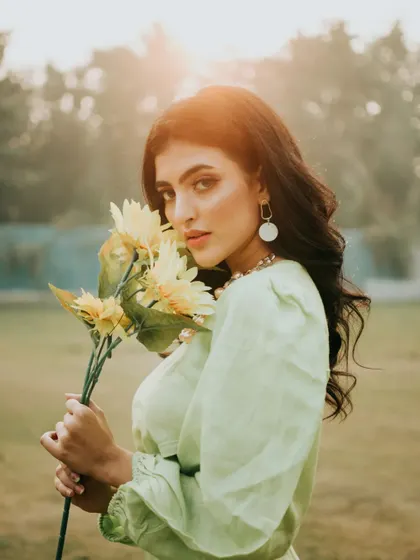 A companion shot to the hero image, this portrait features a direct gaze. The golden backlight and the sunflowers create a warm, inviting, and slightly vintage atmosphere.