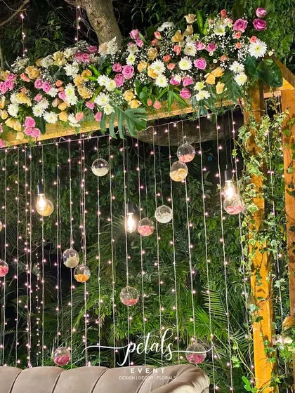 This Jayamala decor is a fairytale dream. The backdrop features a wooden arch adorned with pastel flowers, twinkling fairy lights, and hanging glass bowls filled with petals, creating a whimsical and romantic setting.
