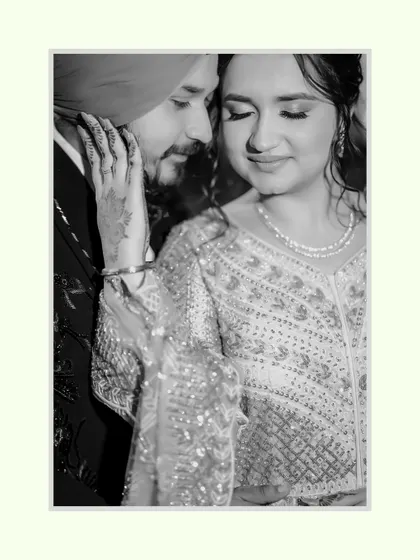 A tender black and white close-up. Ravleen's hand gently caresses Sahib's face, a quiet and powerful expression of love and intimacy captured forever.
