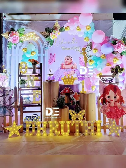 A magical fairy-themed first birthday for Thruth. The stage is lit with marquee letters and star lights, featuring fairy cutouts, a picket fence, and a beautiful balloon arch.