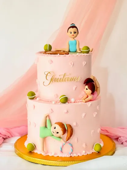 A two-tiered cake for a young gymnast. The pink cake is decorated with fondant figures in various gymnastic poses.