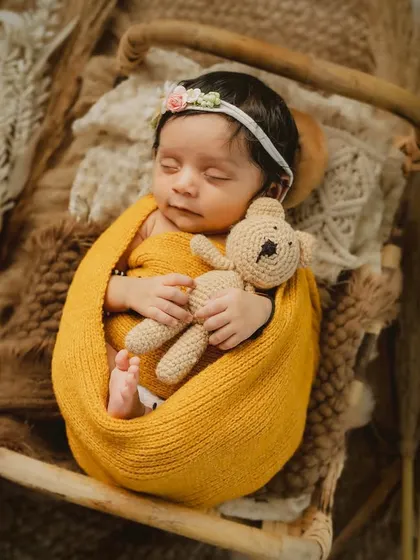 A sleeping baby wrapped in warm, earthy tones for a boho-chic newborn session. The little teddy bear adds a touch of sweetness to this peaceful scene.