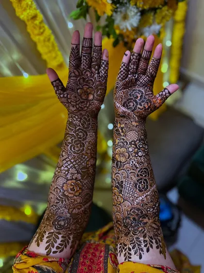 A stunning view of the full bridal floral henna, held up against a festive yellow background. The design is rich with detail.