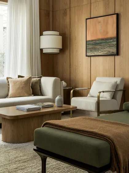 A sophisticated living room with warm wood-paneled walls. The neutral sofa and olive green daybed create a calm and inviting color palette.