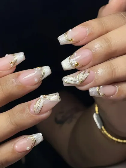 Square-tipped French manicure with 3D gold leaf accents and pearls. This is a modern and luxurious take on a classic style.