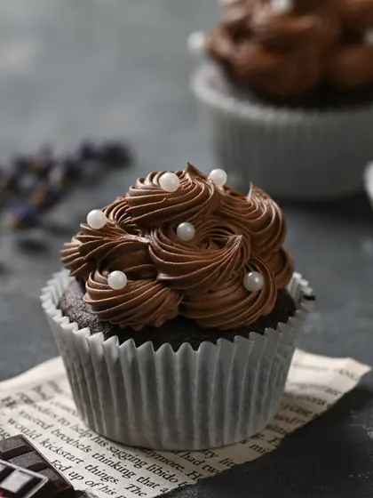 A close-up of our classic eggless chocolate cupcake. It's topped with a rich, swirled chocolate frosting and delicate pearl sprinkles for a simple and elegant finish.