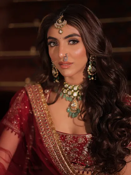 This portrait captures a look of absolute royalty. The deep red lehenga is paired with a heavily layered emerald necklace, a delicate nath, and a maang tikka, creating a powerful and opulent bridal statement.