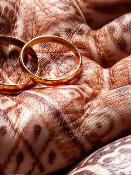 The wedding rings, a symbol of a promise of forever, resting on a hand adorned with mehendi. We help craft and capture these meaningful details of your special day.
