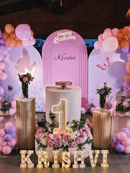 This butterfly-themed first birthday combines soft floral arrangements with a large balloon display. I used a central cake table with a light-up number '1' and the baby's name in marquee letters as the main focus.