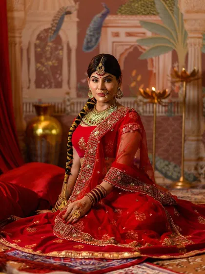 Our recreation of Jodhabai, seated in a regal pose. This image displays the full spread of the embroidered red lehenga against a palatial backdrop, capturing the serene elegance of the Mughal queen.