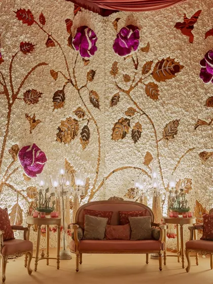 This magnificent stage backdrop is a custom-made flower wall, with a base of white carnations and a design of climbing roses made from purple and metallic-gold dyed petals.