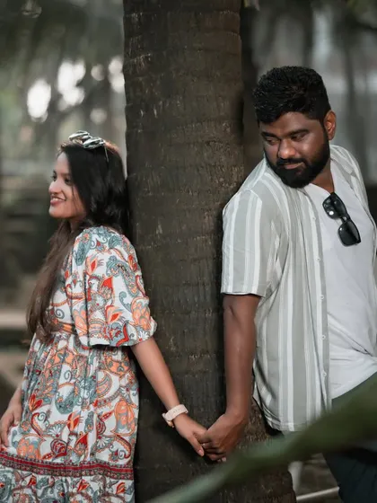 A playful pre-wedding pose with the couple holding hands around a tree trunk, sharing a sweet, stolen glance.