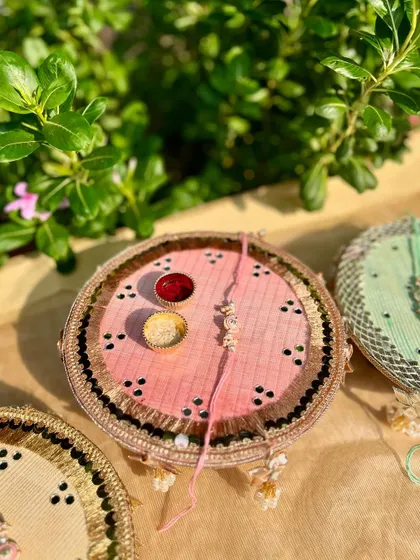 A beautiful pink Rakhi thal with delicate mirror work and a simple, elegant Rakhi, captured in natural light.